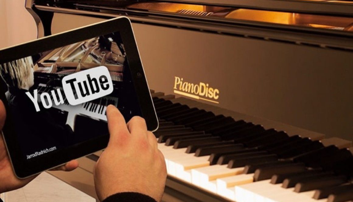 A person holding an ipad in front of a piano.