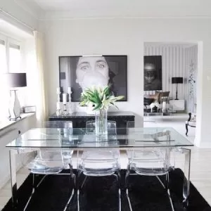 A dining room table with clear chairs and black rug