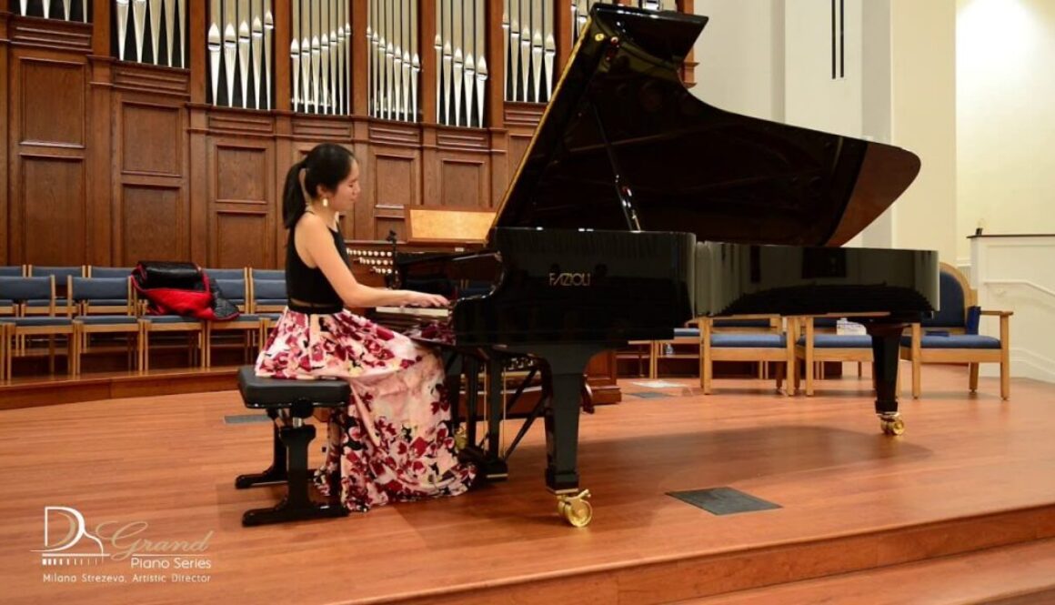 A woman in floral dress playing piano on stage.