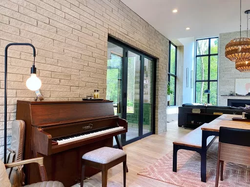 A close up of the piano keys on a Europianos Echo mid century modern upright piano in walnut finish in a Modern living room with large windows.